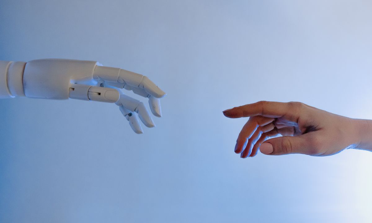 A human hand reaching toward a robotic hand to represent automated collaboration.